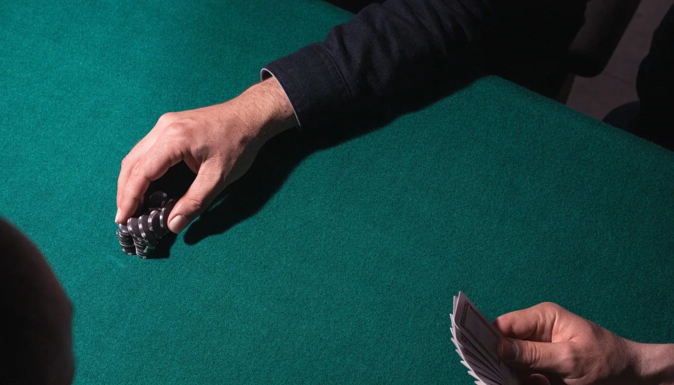 Stół pokerowy w chłodnym świetle — rozdający przesuwa stos żetonów po filcu